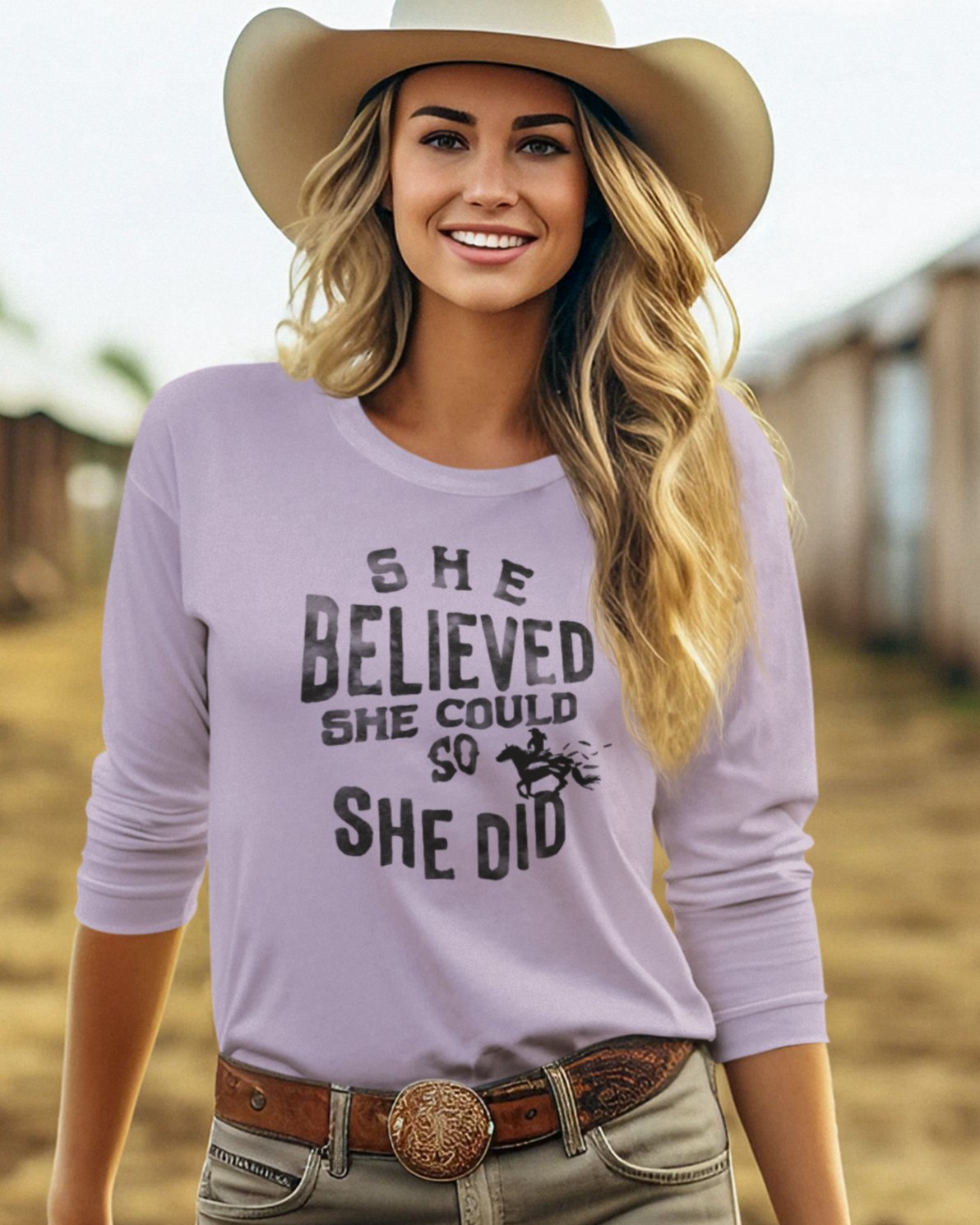 Cowgirl with long blond hair and a cowgirl hat wearing a long sleeve t-shirt that reads "She believed she could so she did". There is a woman riding a horse inside the words.